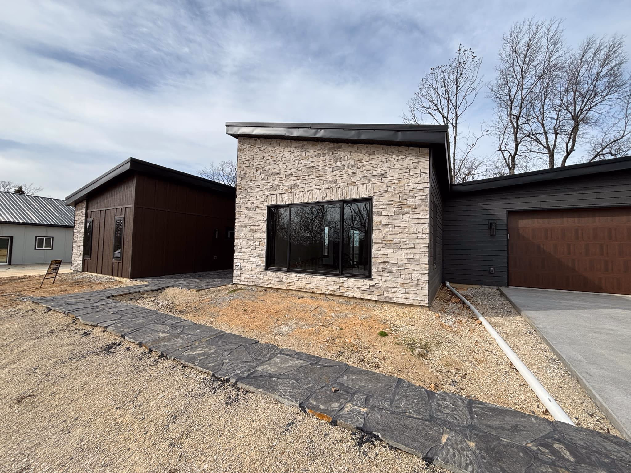 Modern house exterior with stone facade, large window, dark garage door, and a stone pathway.