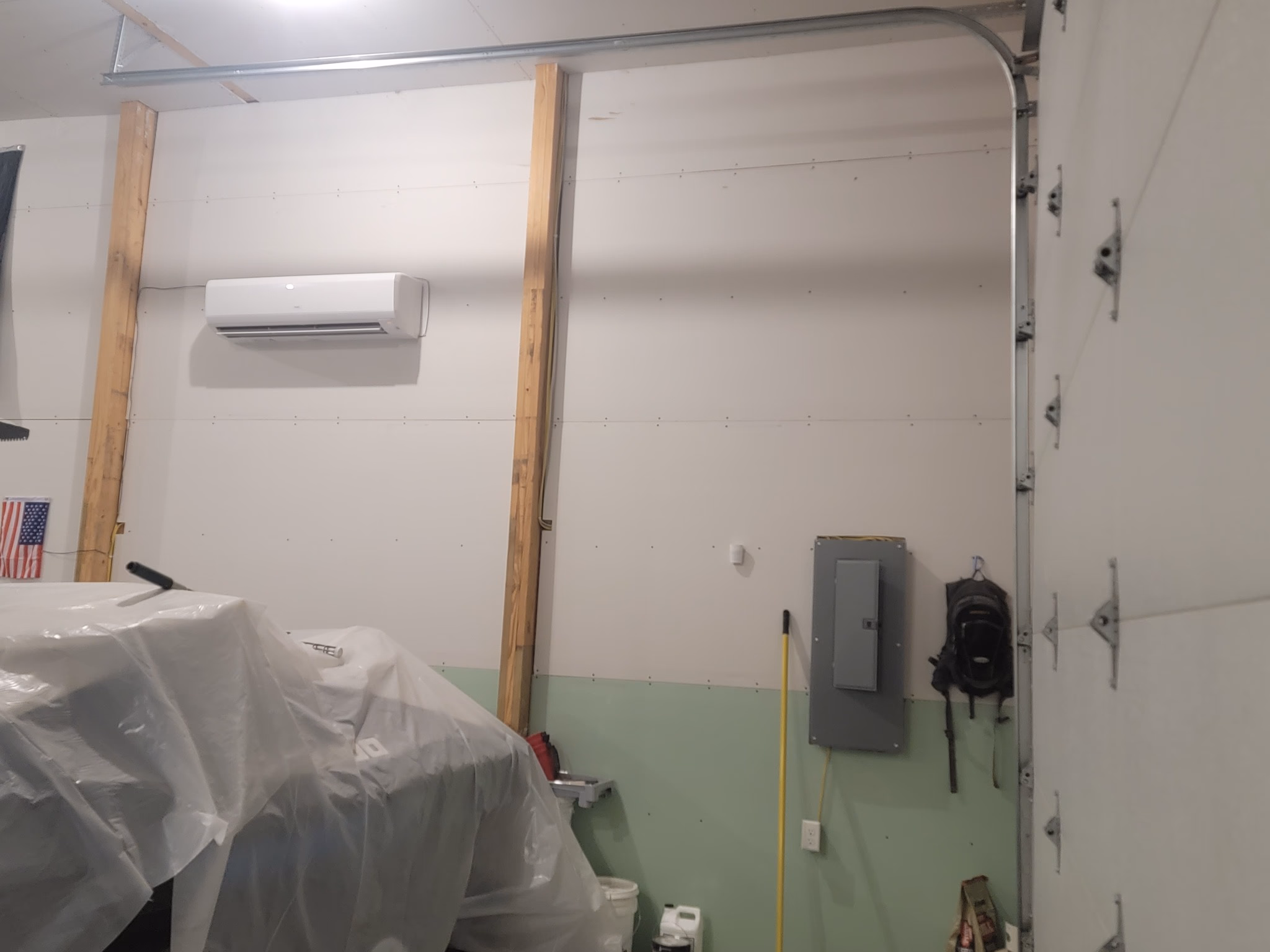 Indoor space with white walls, indoor air conditioner, covered objects, and tools hanging on wall.