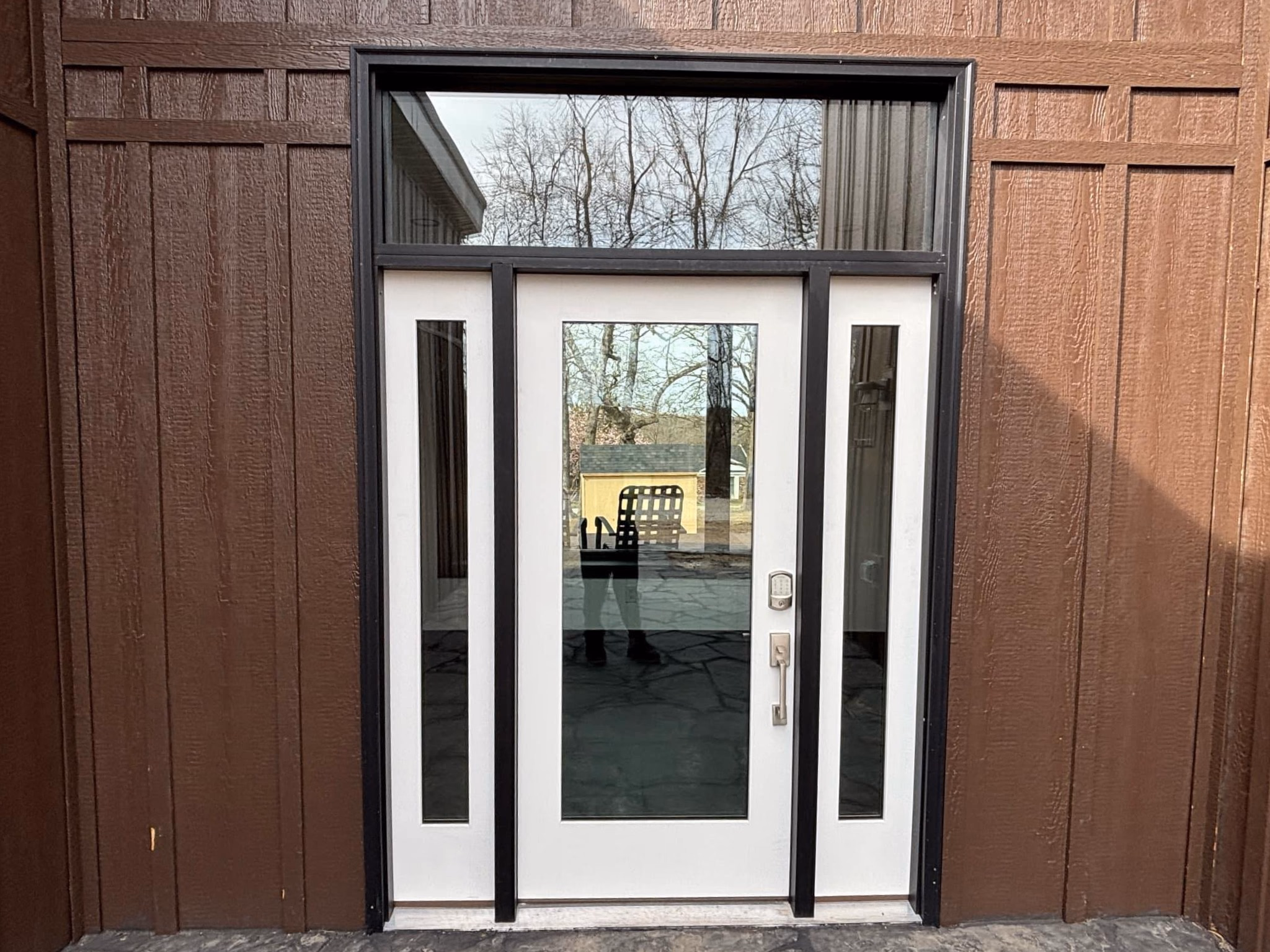 White front door with three vertical glass panels in a brown paneled exterior wall.