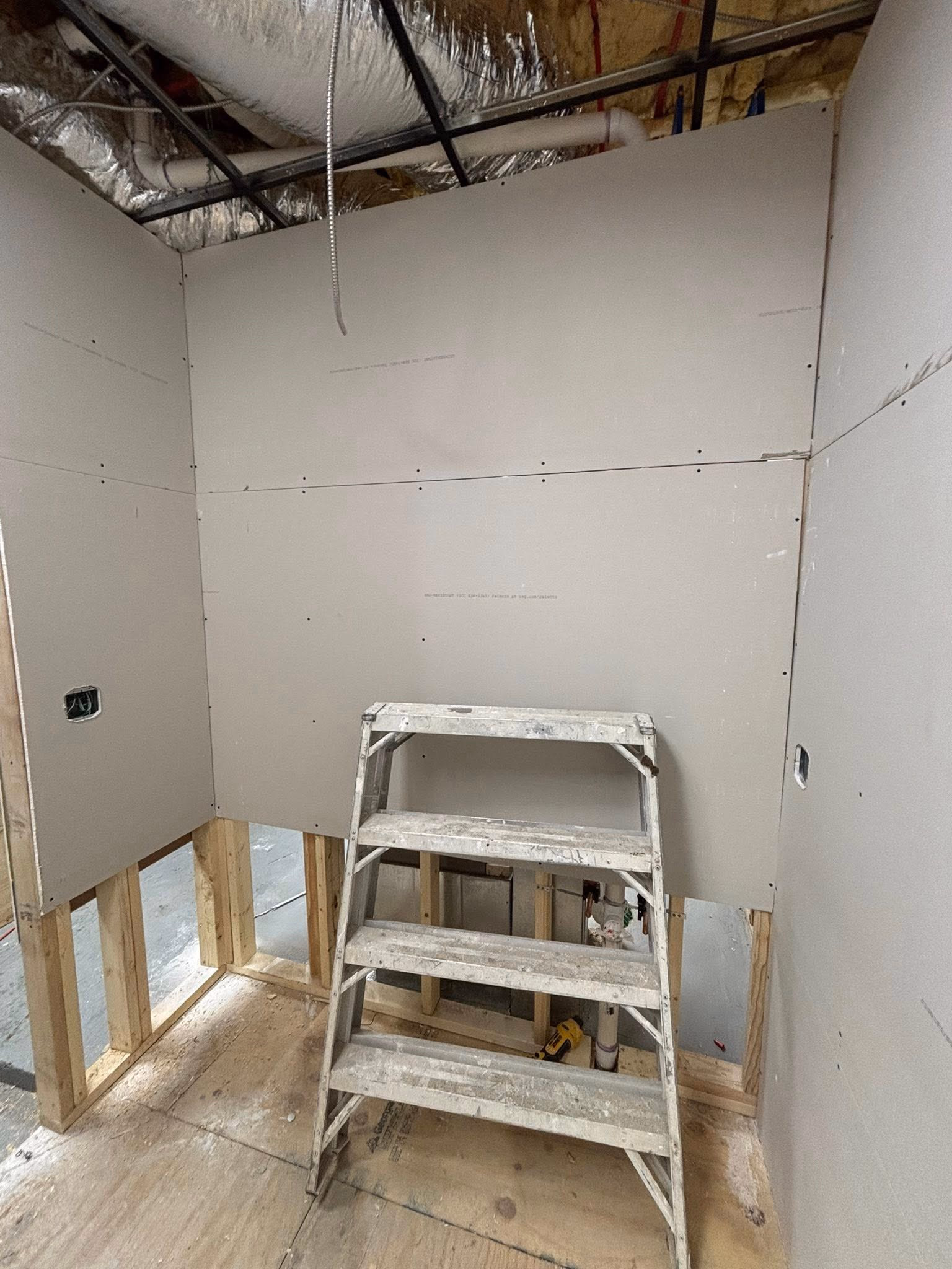 Partially finished room with drywall installed and a paint-splattered step ladder in the center.