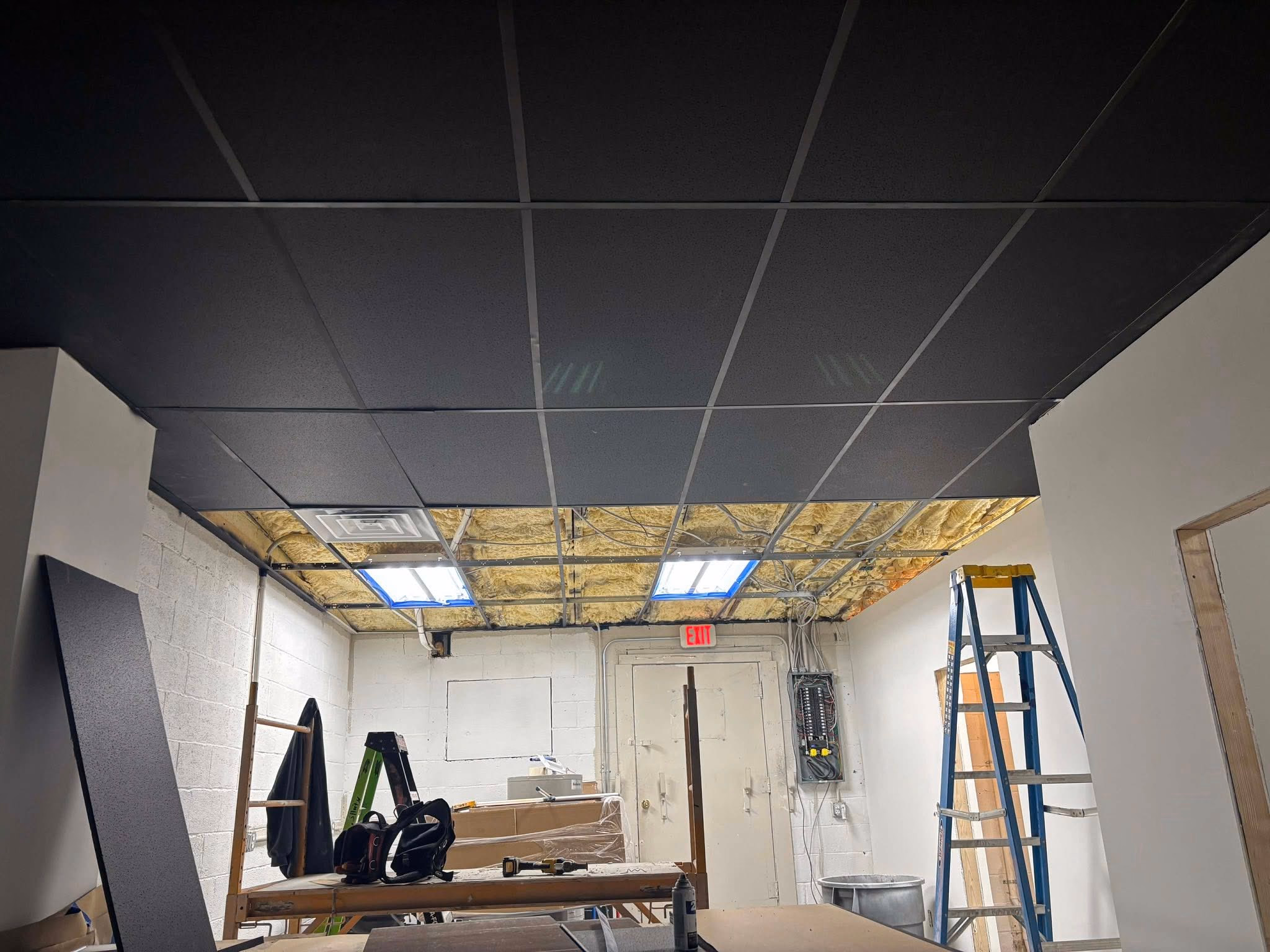 Room under renovation with partially installed drop ceiling and exposed yellow insulation.