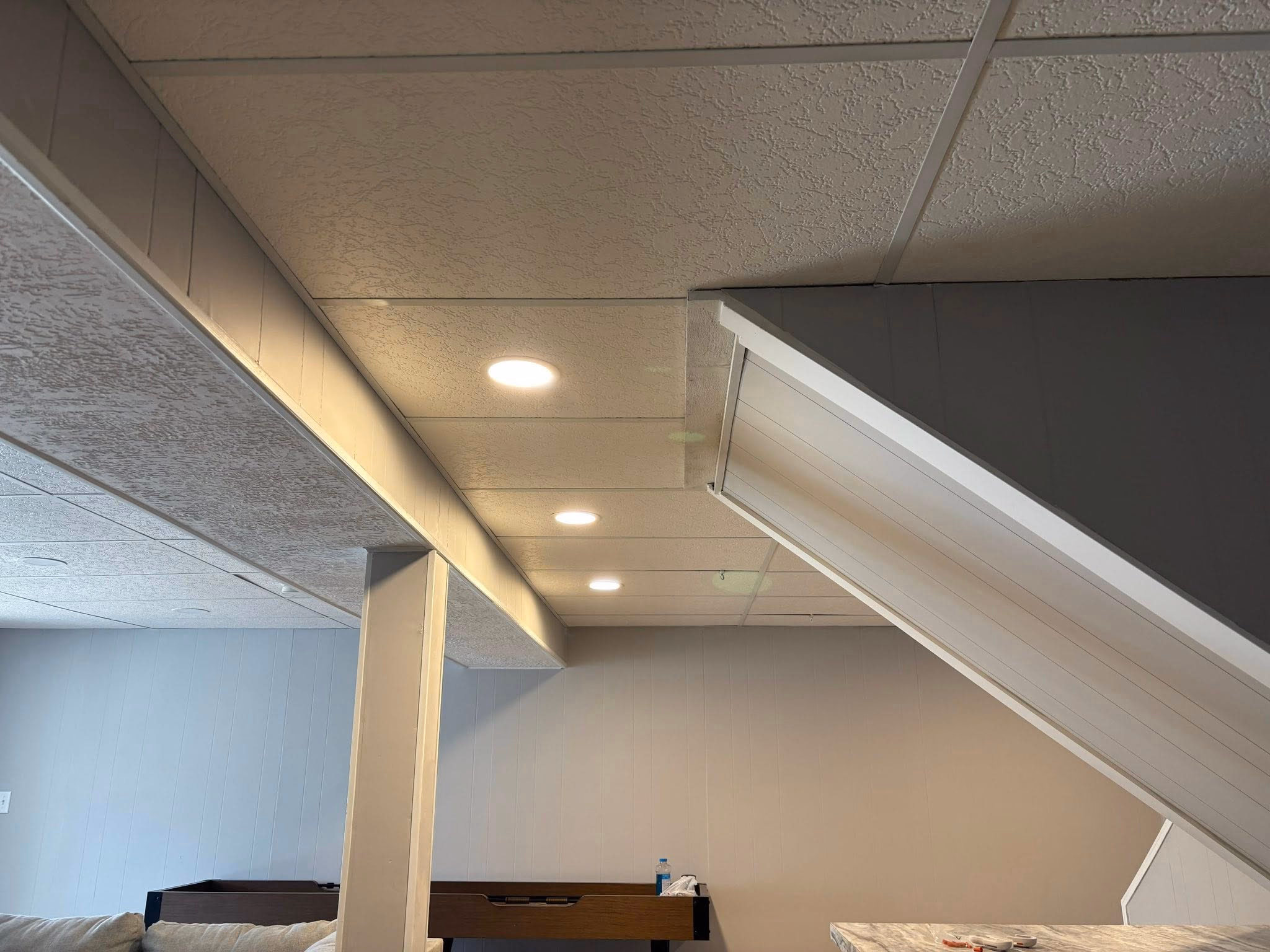 Basement with white textured ceiling, recessed lights, white pillar, and foosball table against wall.