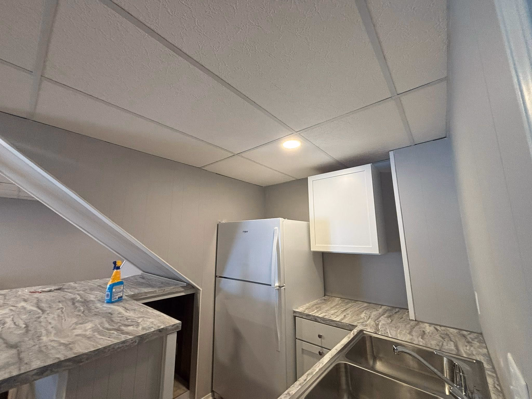 Small kitchen with white cabinets, marble countertop, stainless steel sink, and a white refrigerator.