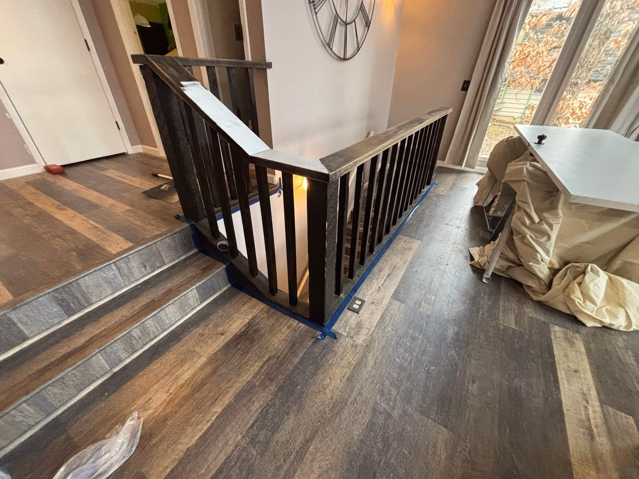 Interior stair railing with dark wood banister, wood-look flooring, and covered furniture near sliding glass door.
