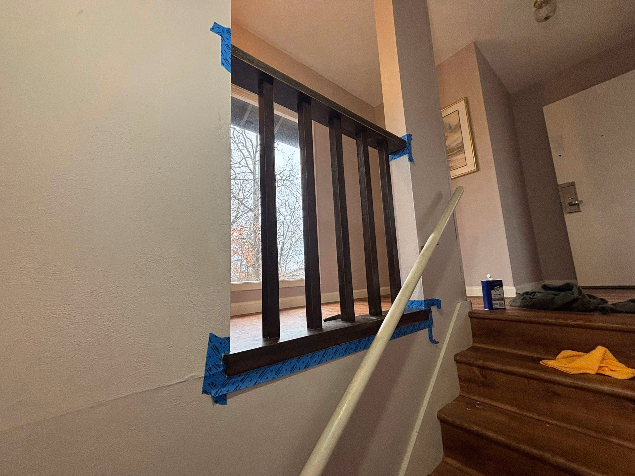 Wooden staircase with dark wooden railing taped for painting or repair near entrance door.
