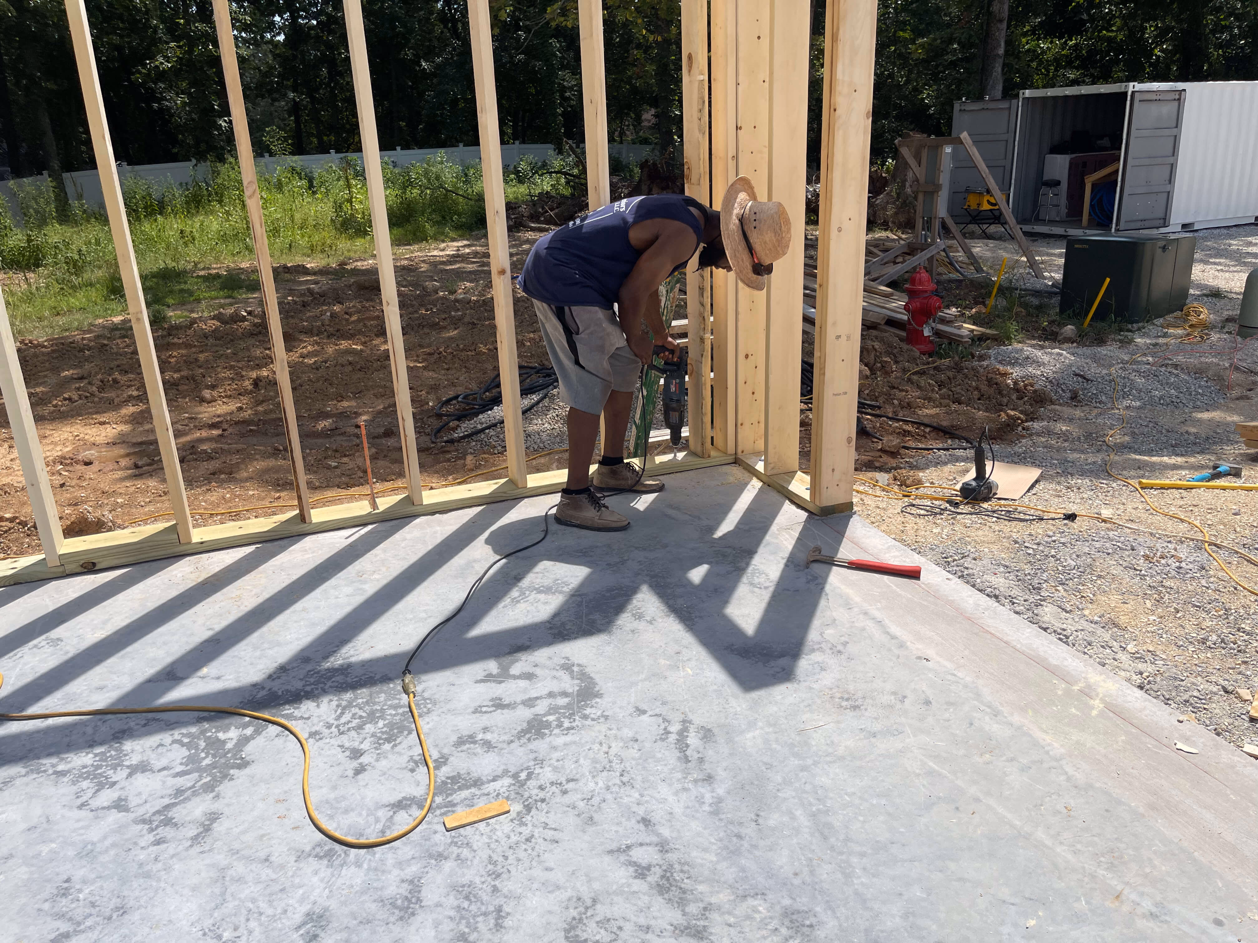 Construction worker with straw hat using power drill on wooden frame of a house under construction.