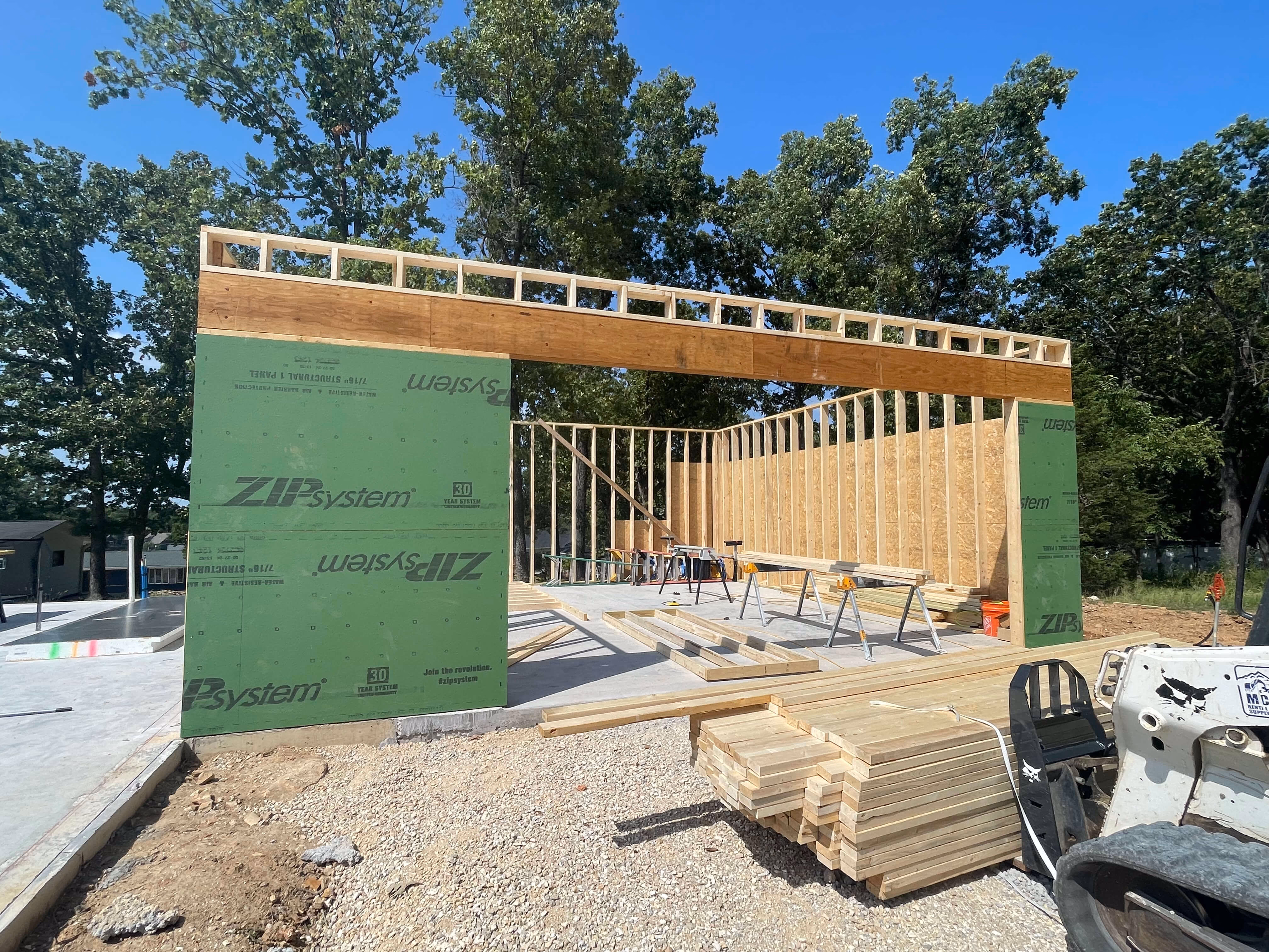 Construction site showing wooden frame and green ZIP system sheathing under a clear blue sky.