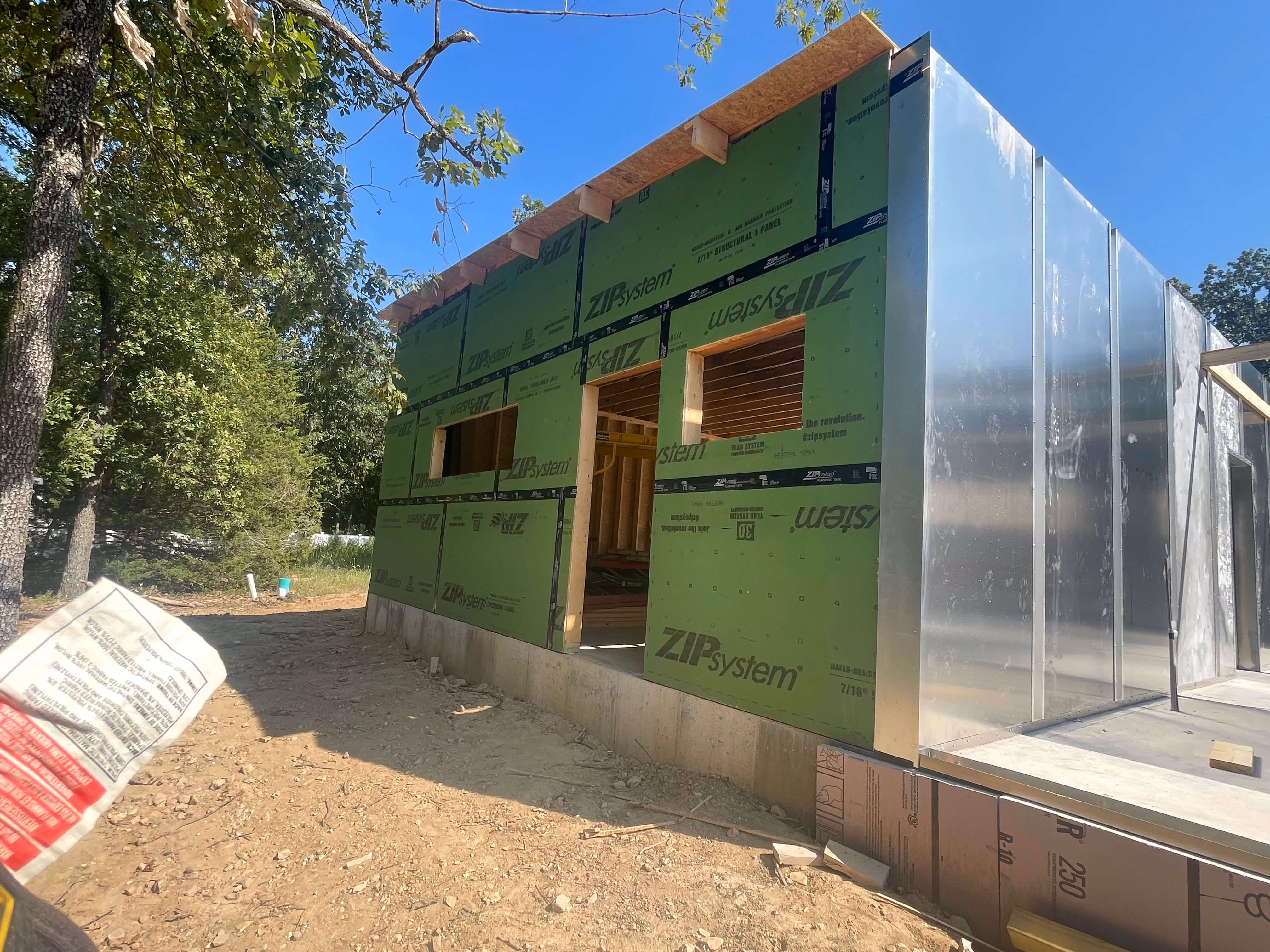Partially constructed building with green ZIP System panels and metal siding under a clear blue sky.