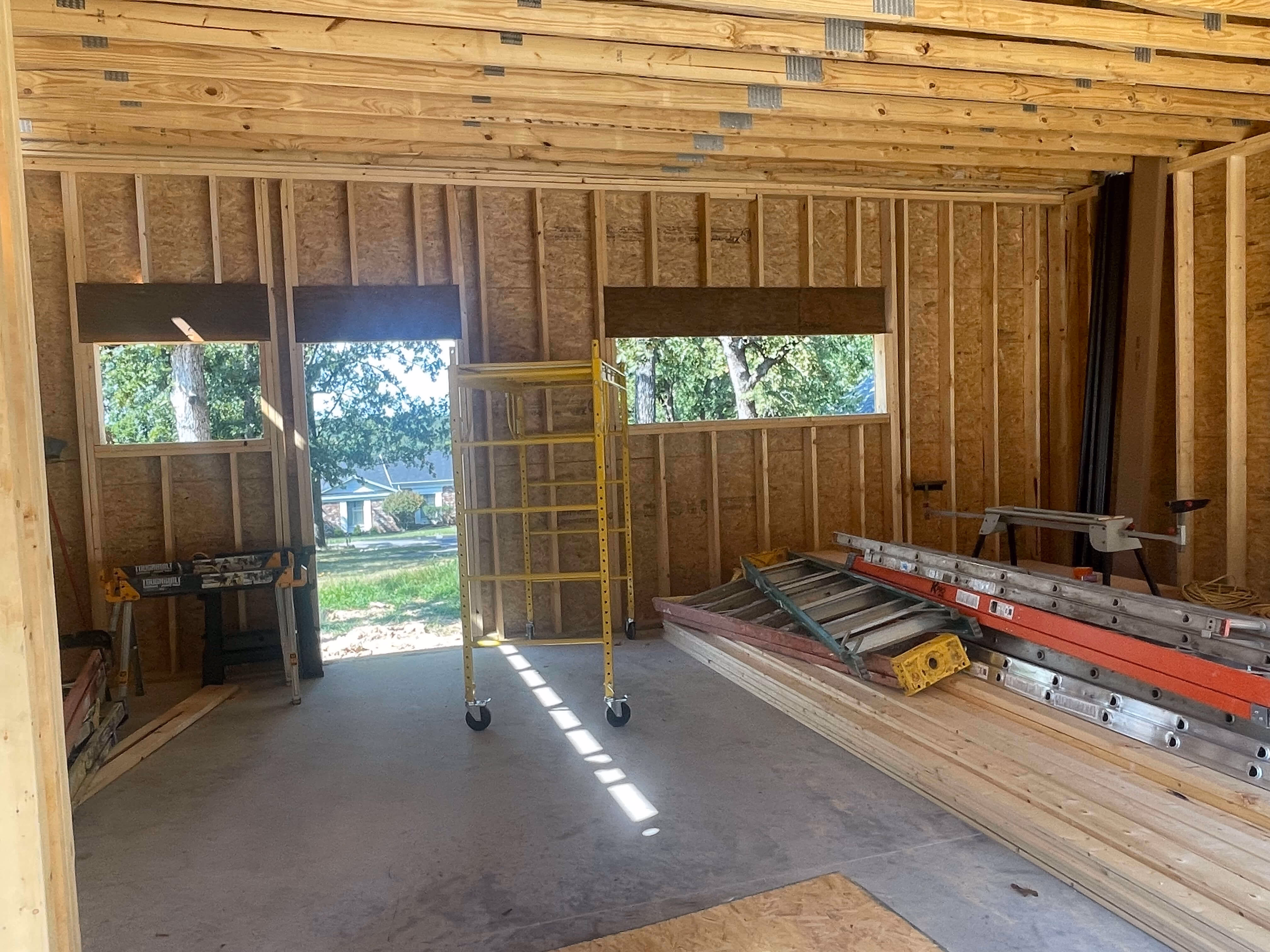 Interior of an unfinished wooden framed room with construction ladders and scaffolding inside.