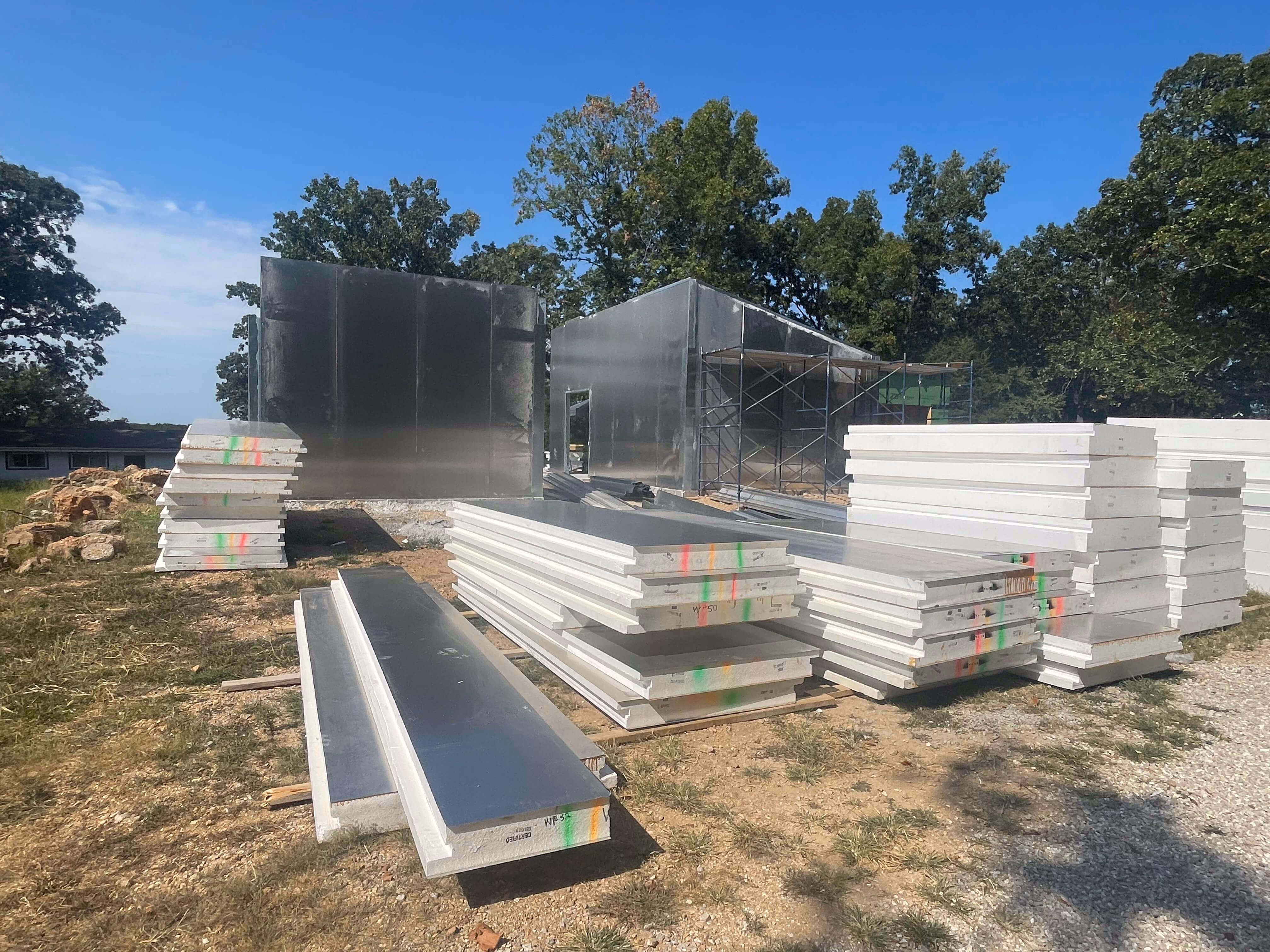 Construction site with stacked insulated metal panels and partially assembled metal building frames.