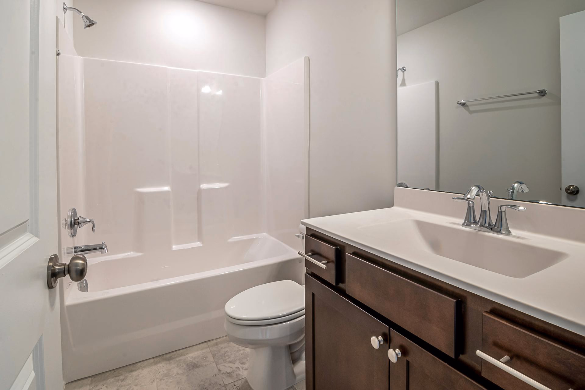 Modern bathroom with white bathtub, toilet, and dark wood vanity with sink and mirror above.
